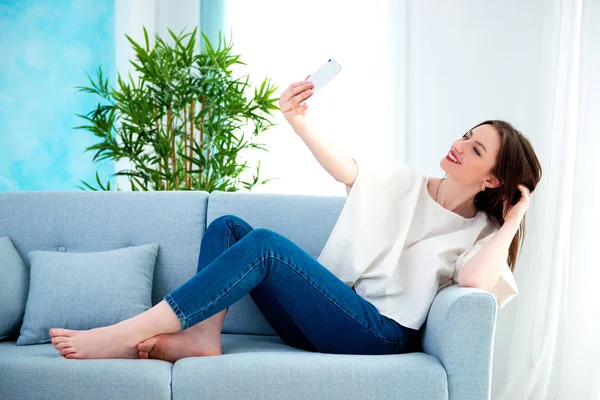 Young brunette girl is making selfie at sofa — Stock Photo, Image