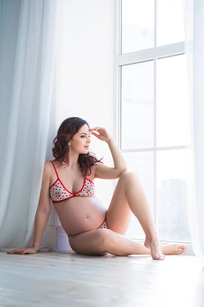 Güzel bir hamile kadın metal-plastik pencere yakınında sıcak bir zeminde oturuyor — Stok fotoğraf