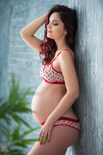 Külot lu hamile kadın ve kalp desenli sütyen saksılı bir çiçekle içeride duruyor. — Stok fotoğraf