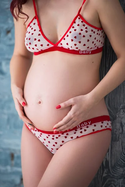 Close-up buik van zwanger meisje in lingerie met een patroon van harten op grijze bakstenen muur achtergrond — Stockfoto
