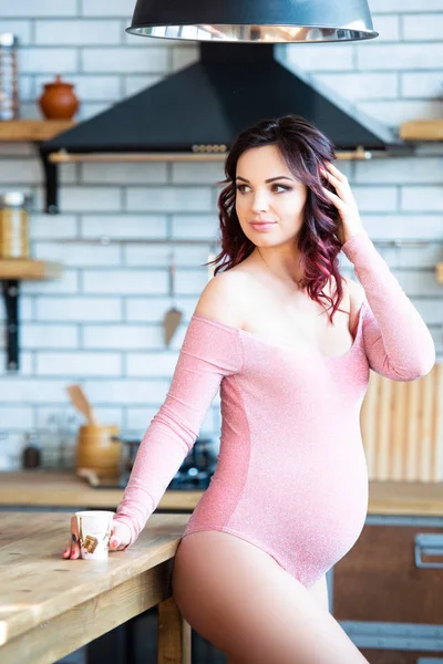 Ung gravid kvinna i rosa body suit dricksvatten i köket. Hur man blir av med morgonillamående och förgiftning. Droger och vitaminer för graviditet — Stockfoto