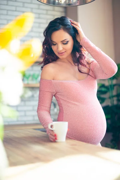 Jonge zwangere vrouw in roze pak drinkwater in de keuken. Hoe om zich te ontdoen van ochtendziekte en toxemie. Geneesmiddelen en vitaminen voor de zwangerschap — Stockfoto