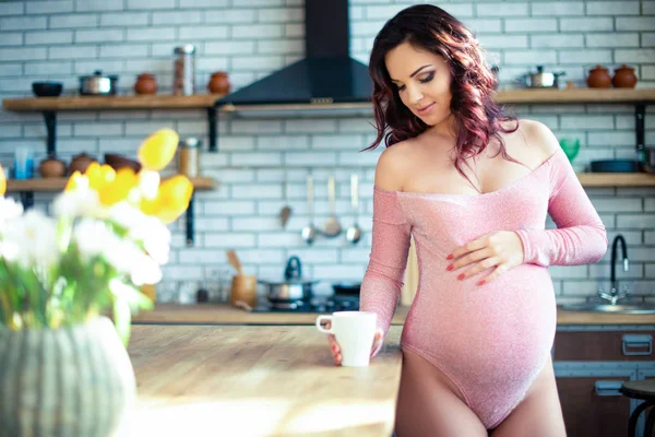 Young pregnant woman in pink bodysuit drinking water in the kitchen. How to get rid of morning sickness and toxemia. Drugs and vitamins for pregnancy — 스톡 사진