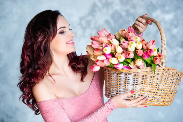 WickerBeautiful young smiling girl with basket of spring flowers of tulips. The best gift is flowers for a birthday and womens day — Stock Photo, Image