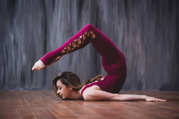 Yoga scorpion pose. Fit sporty girl is stretching. Young beautiful gymnast woman in a jumpsuit doing gymnastic exercises