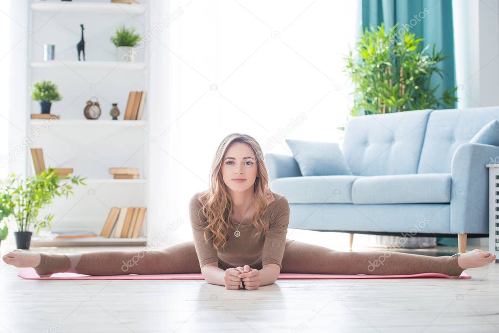 Young fitness beautiful woman female doing sport exercise and sit on splits twine on yoga mat in morning. Healthy lifestyle, morning workout concept