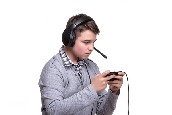 Ragazzo studente adolescente con le cuffie che gioca a un gioco sul cellulare. Gioco d'azzardo, dipendenza dal telefono — Foto Stock