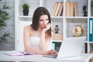 Beyaz bir elbise genç bir esmer kız masada ofiste oturuyor. Kadın laptop çalışıyor