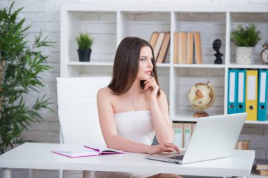 Beyaz bir elbise genç bir esmer kız masada ofiste oturuyor. Kadın laptop çalışıyor