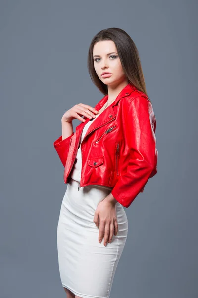 Stile alla moda, moda abbigliamento femminile, combinazione di colori. Bella ragazza bruna in abito bianco e giacca di pelle rossa isolato sfondo grigio — Foto Stock