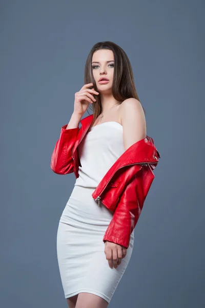 유행 스타일, 패션 여성의 의류, 색상 조합. 아름 다운 갈색 머리 소녀 에 화이트 드레스 와 빨간 가죽 재킷 고립 된 회색 배경 — 스톡 사진