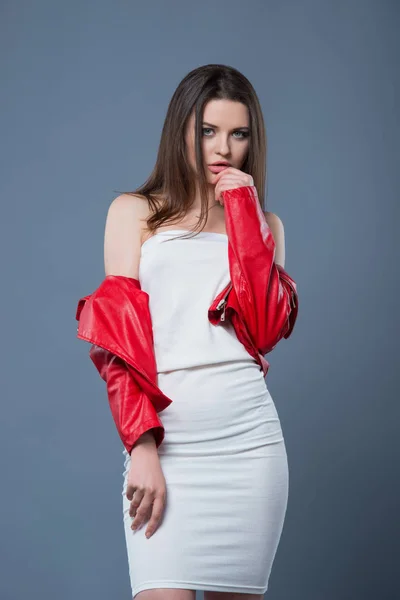Fashionable style, fashion women's clothing, color combination. Beautiful brunette girl in white dress and red leather jacket isolated gray background — Stock Photo, Image