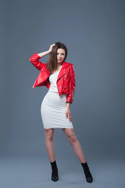 Fashionable style, fashion women's clothing, color combination. Beautiful brunette girl in white dress and red leather jacket isolated gray background — Stock Photo, Image