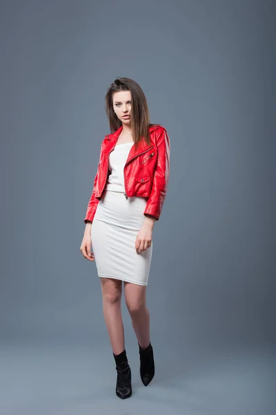 Estilo de moda, ropa de mujer de moda, combinación de colores. Hermosa chica morena en vestido blanco y chaqueta de cuero rojo fondo gris aislado — Foto de Stock