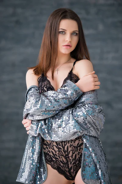 Bella ragazza bruna sexy in abito di pizzo nero e giacca d'argento si erge contro lo sfondo grigio muro di mattoni — Foto Stock