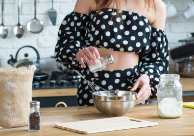 Puantiyeli elbisesiyle güzel bir esmer kız mutfaktaki ahşap masada yemek pişiriyor. Yemek pişirmeye yakın.