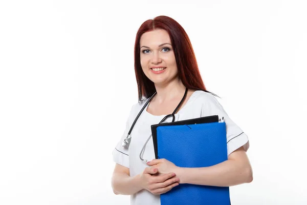 Szczęśliwa młoda kobieta lekarz rodzinny posiada niebieski folder z dokumentami, ma przyjazną ekspresję, izolowane białe tło. Koncepcja medycyny — Zdjęcie stockowe