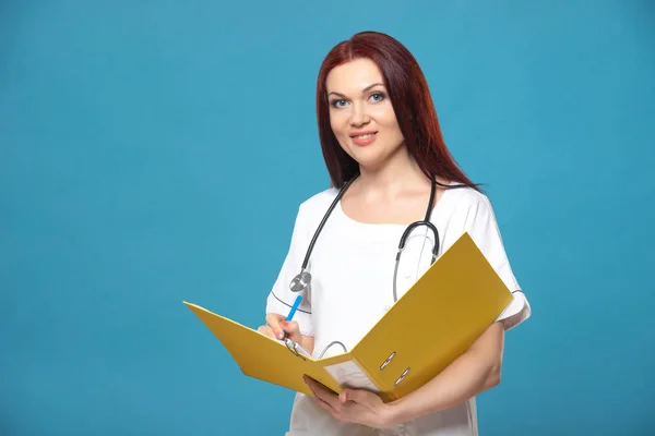 Family female woman doctor with a stethoscope holds folder with documents, has friendly expression, isolated blue background. Medicine concept