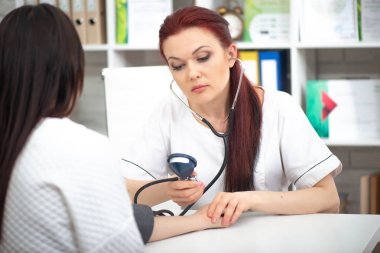 Gülümseyen dost bir doktor ofisinde bir hasta alır ve basıncı ölçer. Kadın tıbbi tavsiye verir
