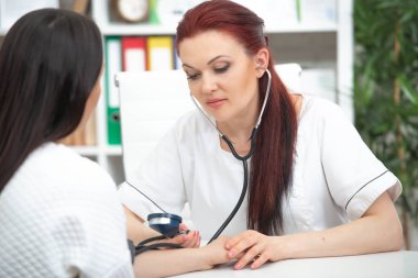 Gülümseyen dost bir doktor ofisinde bir hasta alır ve basıncı ölçer. Kadın tıbbi tavsiye verir