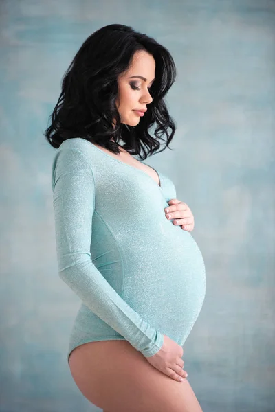 Krásná těhotná dívka Bruneta žena v módním modrém obleku stojí u zdi. Koncept zdravého těhotenství a šťastné mateřství — Stock fotografie