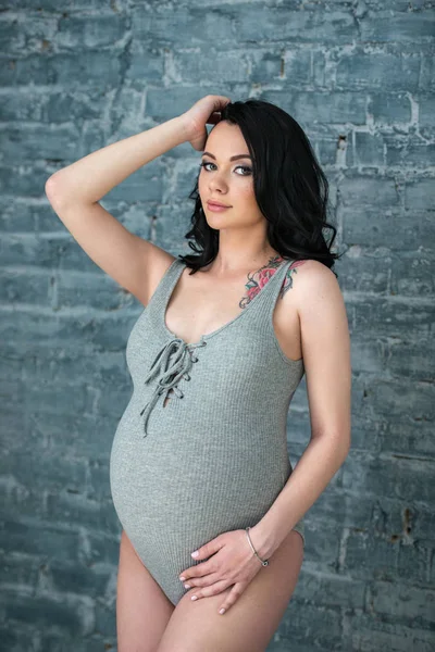 Těhotná dívka Bruneta v pleteném obleku stojí na pozadí šedé cihlové zdi. Styl a těhotenství podkroví — Stock fotografie