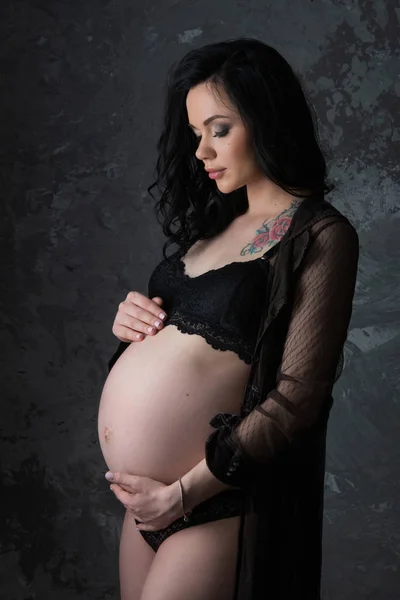 Koncepcja ciąży. Piękna kobieta w ciąży w czarnej bieliźnie przytulania jej brzuch na ciemnym tle — Zdjęcie stockowe