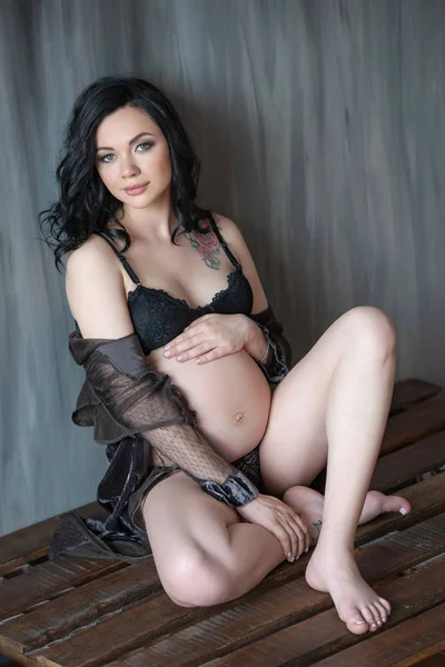 Belle femme brune enceinte assise sur une palette en bois près du mur — Photo