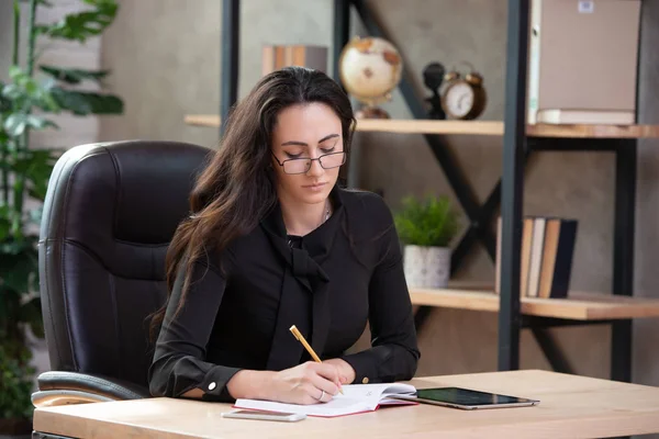 Beautiful stylish business woman with glasses sitting in an office at the table — Stock Photo, Image