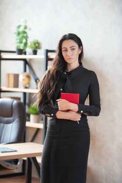 Die schöne, stylische Geschäftsfrau mit einem roten Notizbuch in der Hand steht im Büro. Wirtschaft und Karriere von Frauen — Stockfoto