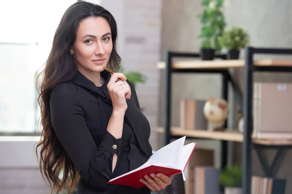 Beautiful stylish business woman in the office makes important entries in a red notepad. Female business planning and career growth — Stock Photo, Image
