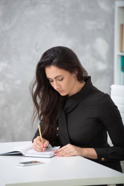 Bir iş siyah elbiseli bir esmer kız ofiste bir masada oturuyor ve çok çalışıyor. Öğrenci not yazar, not defterine notlar alır