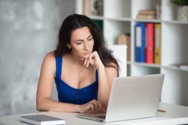 Mavi elbiseli güzel iş kadını tasarımcı dizüstü bilgisayara bakıyor. Ofiste kadın iş