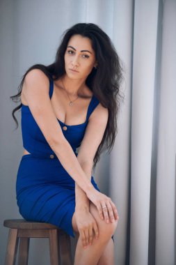 İşyerinde ofis romantizmi. Ahşap bir taburede oturan mavi elbiseli baştan çıkarıcı iş kadını sekreteri