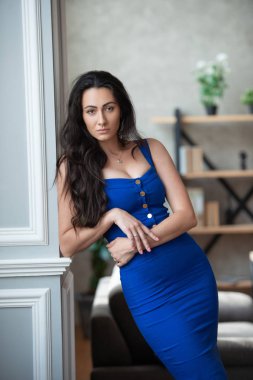 Mavi elbiseli güzel iş kadını ofis odasında sütun yakınında duruyor