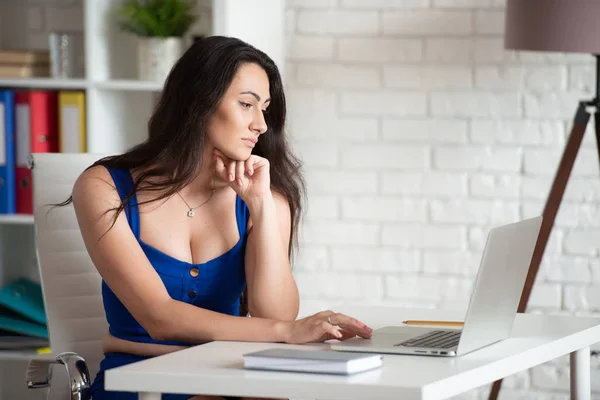 Hermosa diseñadora de mujer de negocios en vestido azul mira en el portátil. Negocio femenino en la oficina —  Fotos de Stock