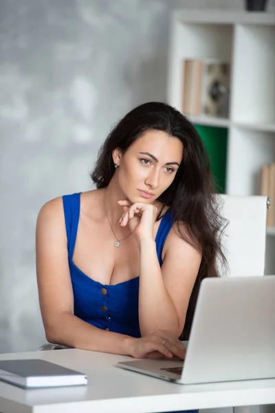 Piękne biznesmen projektant w niebieskiej sukni patrzy do laptopa. Kobieta biznesu w biurze — Zdjęcie stockowe