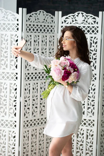 Embarazo saludable y maternidad feliz. Hermosa joven embarazada con un ramo de flores hace selfie — Foto de Stock