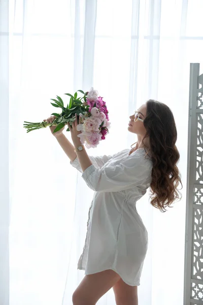 Hermosa joven embarazada con un ramo de flores contra la ventana — Foto de Stock