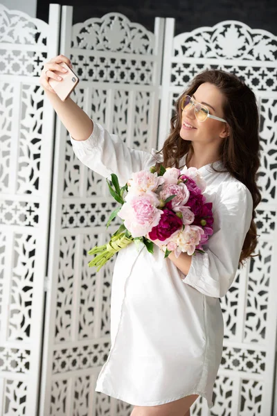 Gravidez saudável e maternidade feliz. Bela jovem grávida com um buquê de flores faz selfie — Fotografia de Stock