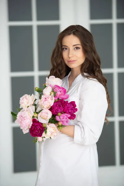 ゴージャスな髪とピオニーの花の花束を持つ美しい若い女性の女の子のクローズアップ肖像画 — ストック写真