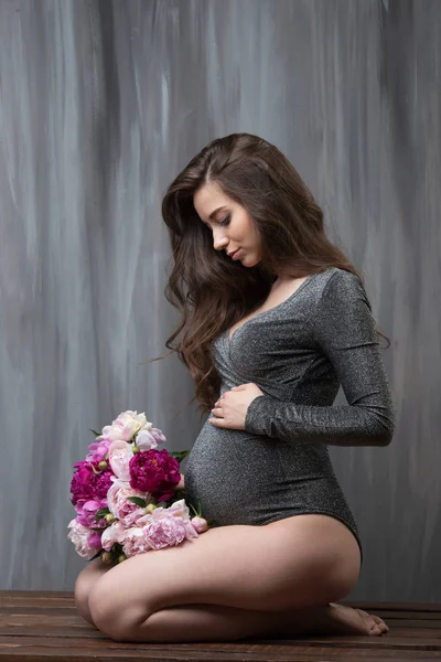 Όμορφη νεαρή έγκυος γυναίκα με μια ανθοδέσμη παιώνιες λουλουδιών. Το κορίτσι έχει μακριά κυματιστά μαλλιά — Φωτογραφία Αρχείου