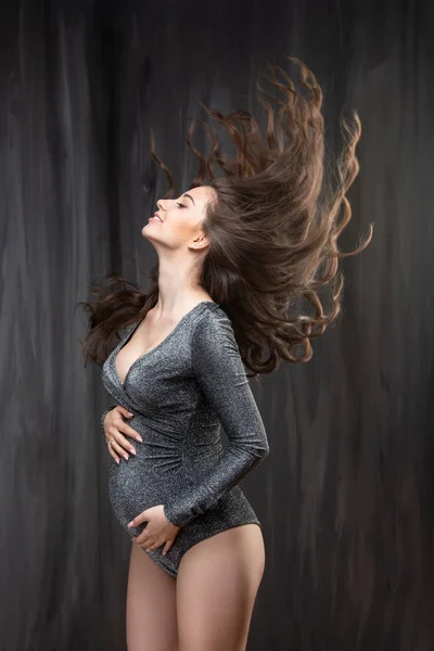 Mulher grávida bonita com espalhando cabelo ondulado longo contra uma parede de concreto cinza. vento soprando cabelo — Fotografia de Stock