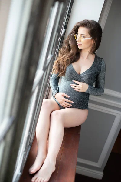 Schöne schwangere Frau mit Brille sitzt in der Nähe des Fensters im Inneren des Zimmers. Gesundes Sehvermögen und Schwangerschaft — Stockfoto