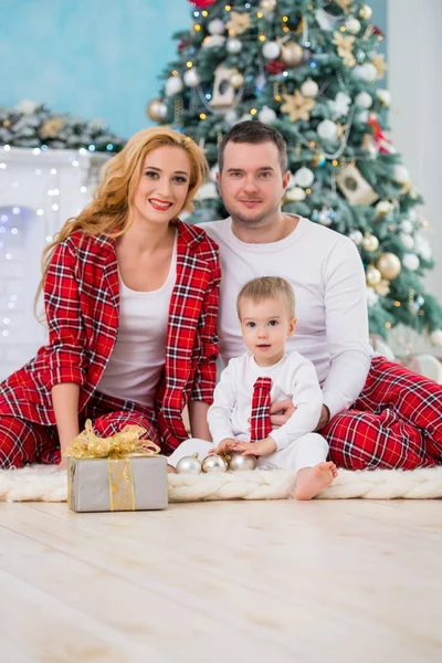 Felice famiglia sorridente in pigiama a scacchi vicino all'albero di Natale e al camino di Capodanno — Foto Stock