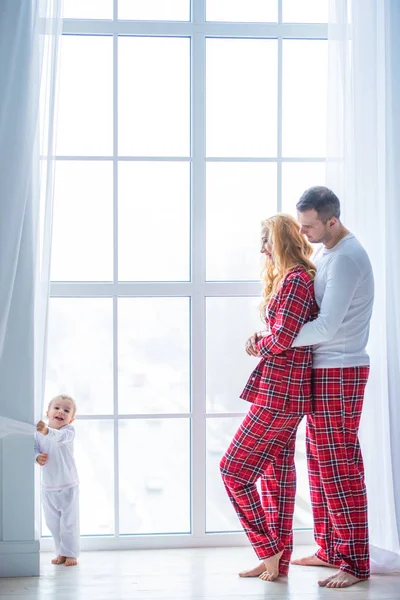 Щаслива сім'я стоїть біля величезного сучасного пластикового вікна. Мати, батько і маленький син одягнені в піжаму — стокове фото