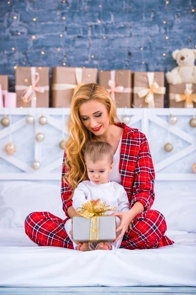 Мати в картатій піжамі і маленький син відкривають подарунок на Новий рік разом — стокове фото