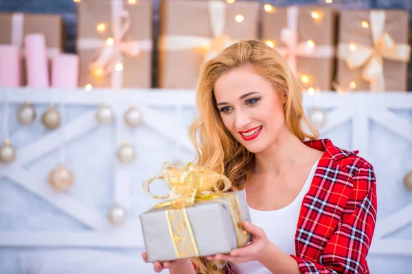 Schöne junge blonde Frau im karierten Pyjama mit Neujahrsgeschenken. Frohe Weihnachten und ein gutes neues Jahr — Stockfoto