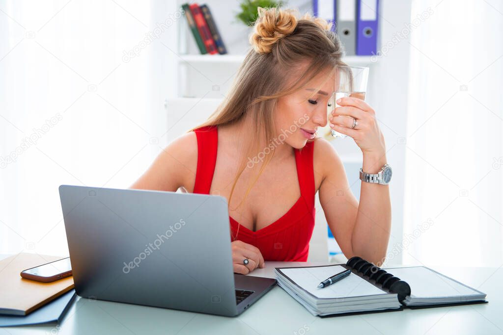 Young woman sitting in office at computer with a glass of clean water. Drinking plenty is the key to health, helps with stress and fatigue in business