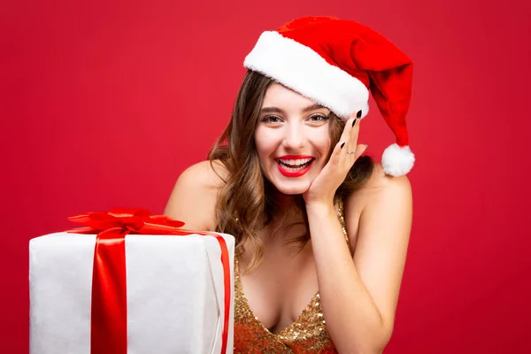 Hermosa chica sexy de Santa en oro elegante vestido de noche y sombrero de Navidad con un regalo de Año Nuevo en las manos. Emociones felicidad y deleite. Cara sonriente —  Fotos de Stock